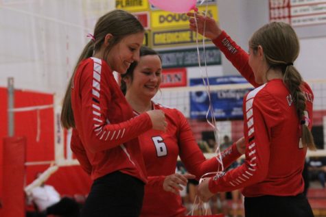 During senior night, senior Karley Mooneyham is given a gift by junior Kyla Echelberry and sophomore Kenzie Wenke. “I feel bittersweet because I’m pretty done with high school, but I loved volleyball and have played it for a long time,” Mooneyham said.