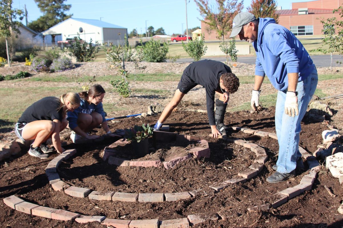 Senior Haylee Osner, and sophomores Morgan Koester and Eli Benge help Mr. Bellar lay bricks around the pollinator garden. This was a project for the Advanced Biology class. 